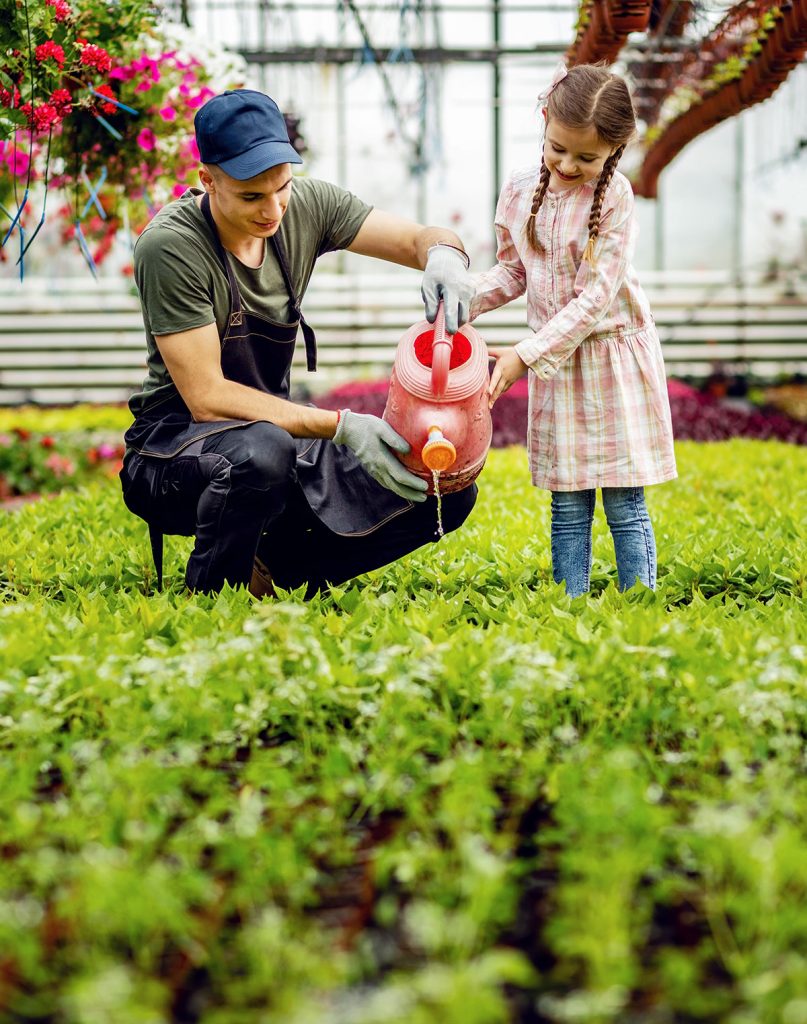 Photo d'un jardinier et d'une petite fille en train d'arroser des plants
